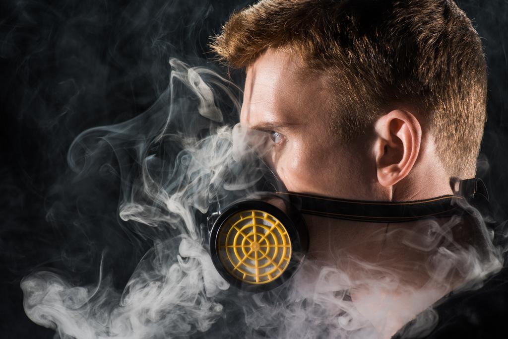 Человек в черном капюшоне в защитной фильтрующей маске, окруженный облаками дыма
 - Фото, изображение