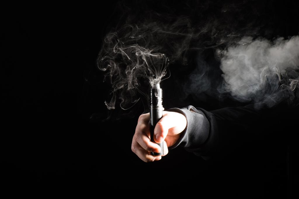 Обрезанный вид мужской руки, активирующей электронную сигарету на черном фоне
 - Фото, изображение