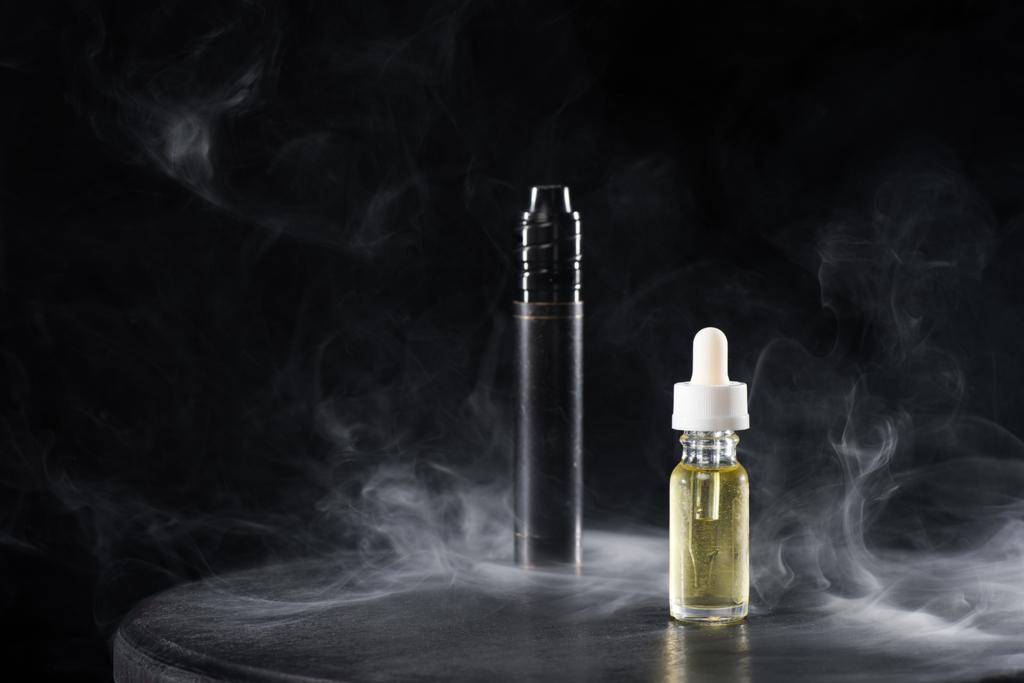 Elektronische Zigarette und Flüssigkeit mit Rauchwolken auf dunklem Hintergrund - Foto, Bild