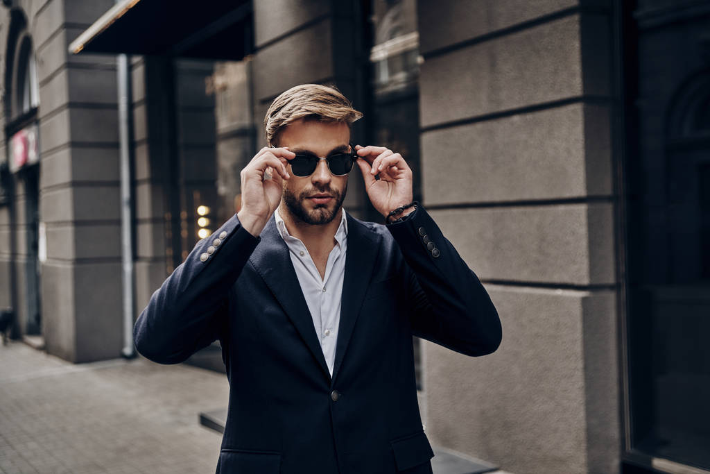 Όμορφος νεαρός άνδρας smart casual ντύσιμο προσαρμογή γυαλιά, ενώ το περπάτημα στο δρόμο της πόλης - Φωτογραφία, εικόνα