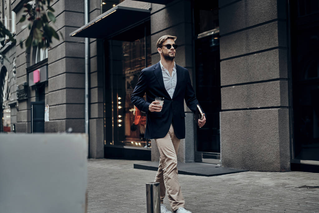 Przystojny biznes człowiek przenoszenia jednorazowego kubka z kawą podczas spaceru w ulicy miasta - Zdjęcie, obraz