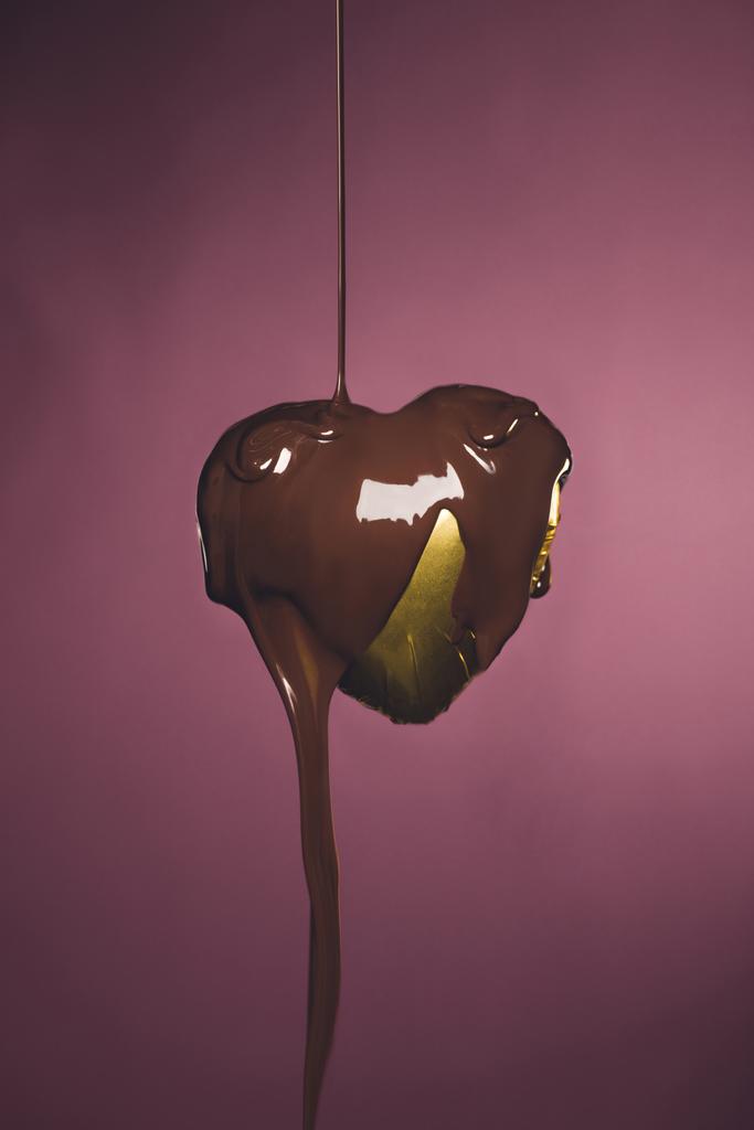 hart vormige snoep in gouden wrapper met vloeibare chocolade geïsoleerd op roze - Foto, afbeelding