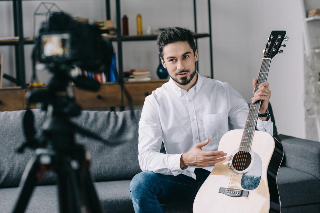 guapo bloguero de música sosteniendo y describiendo la guitarra acústica
  - Foto, imagen