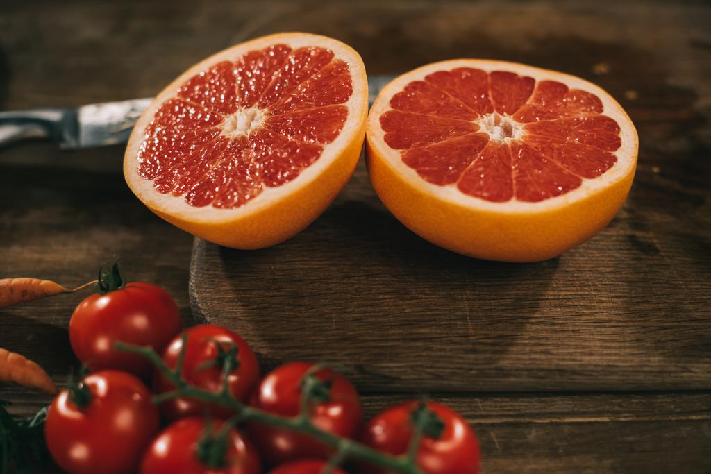 toronja cortada sobre tabla de madera y tomates cherry sobre mesa
 - Foto, Imagen