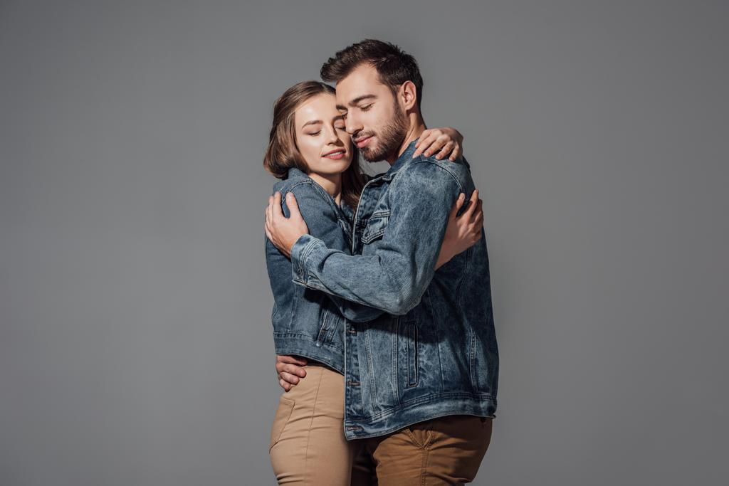 glückliches junges Paar mit geschlossenen Augen, die sich isoliert auf grau umarmen - Foto, Bild