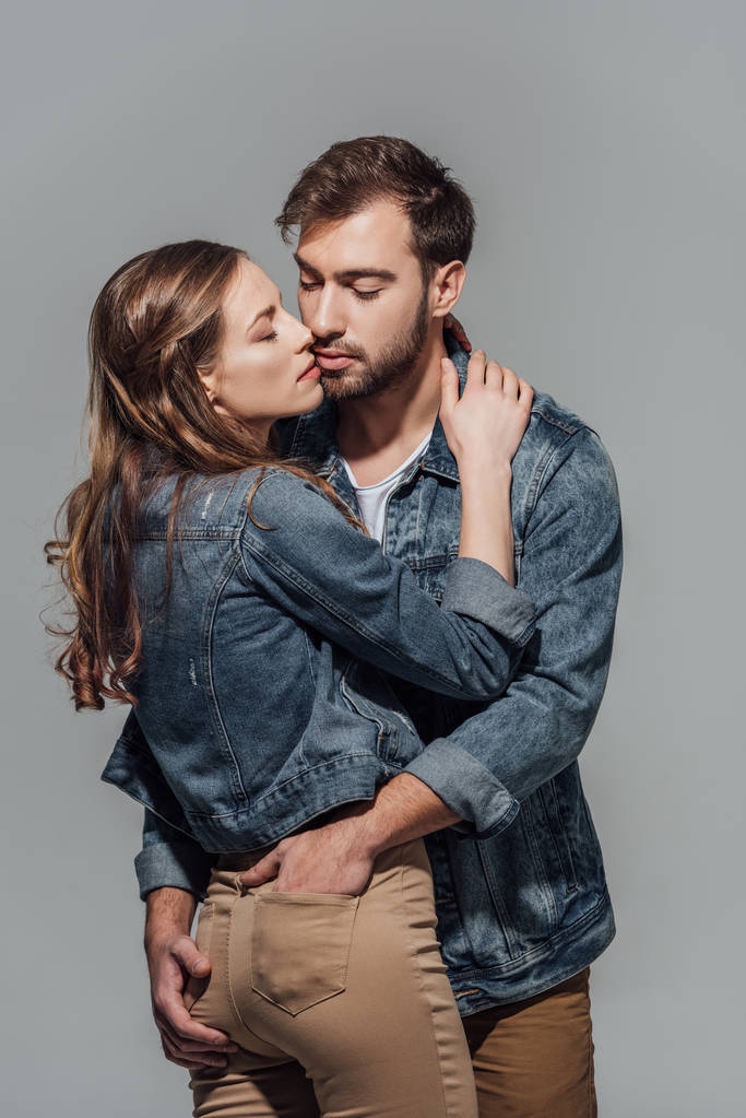 σαγηνευτικό νεαρό ζευγάρι στο τζιν μπουφάν αγκάλιασμα απομονώνονται σε γκρι - Φωτογραφία, εικόνα