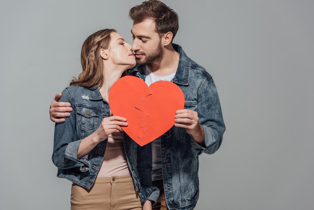 傷ついた心の部分を保持している若いカップルは一緒に記号し、グレーに分離されたキス - 写真・画像
