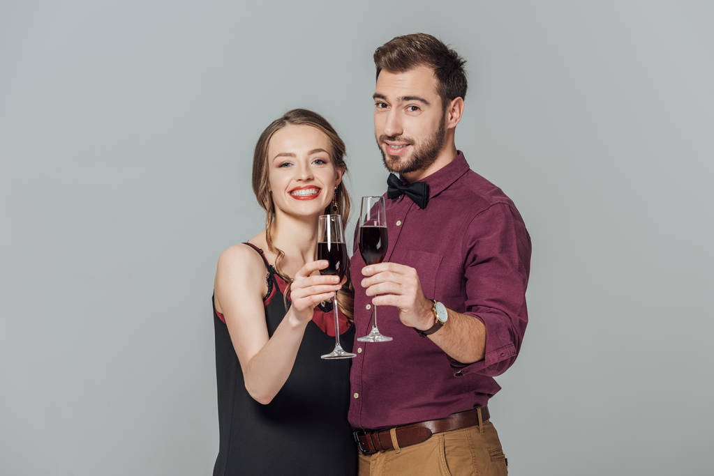 beau jeune couple élégant tenant des verres de vin rouge et souriant à la caméra isolé sur gris
 - Photo, image