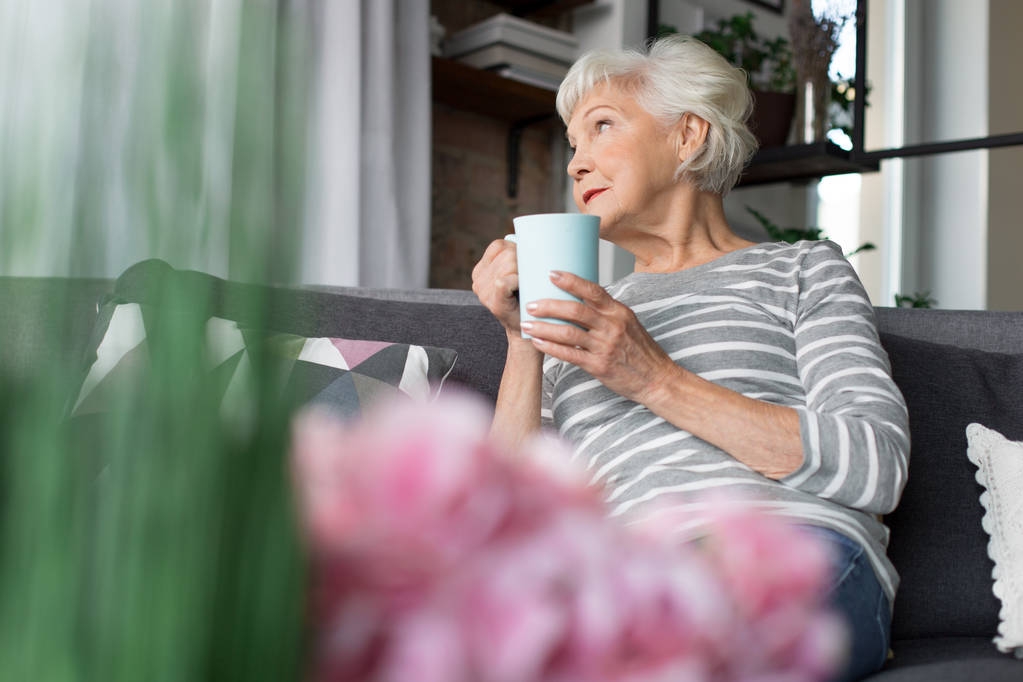 Charming old woman relaxing on couch with hot drink - Photo, Image