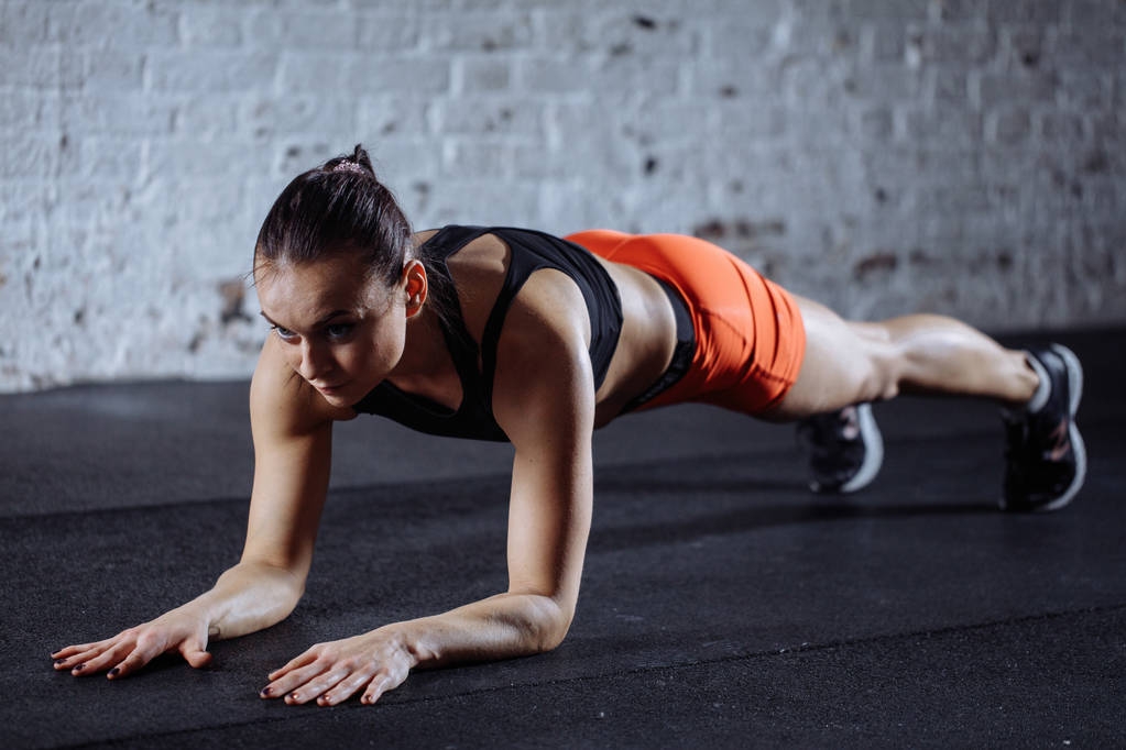 beautiful woman in sportswear doing plank while trainnig at cross fit gym - Photo, Image
