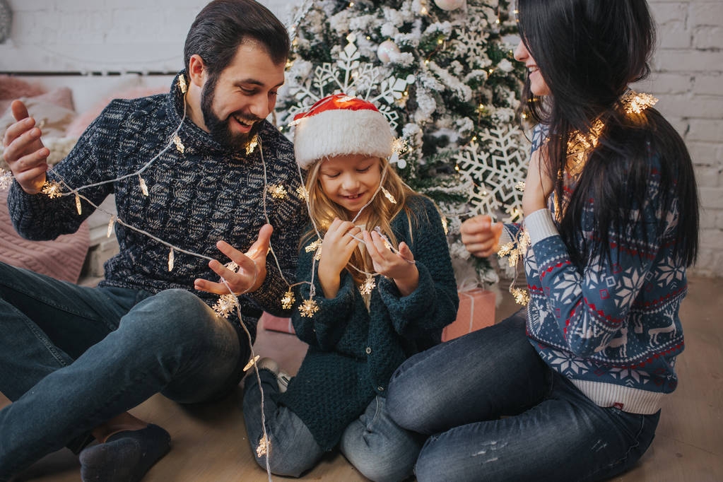 Beautiful young family enjoying their holiday time together, decorating Christmas tree, arranging the christmas lights and having fun - Photo, Image