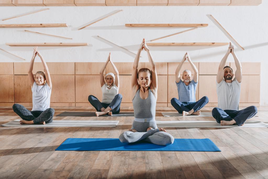 Seniorengruppe praktiziert Yoga mit Instruktor in Lotus-Pose auf Matten im Studio - Foto, Bild