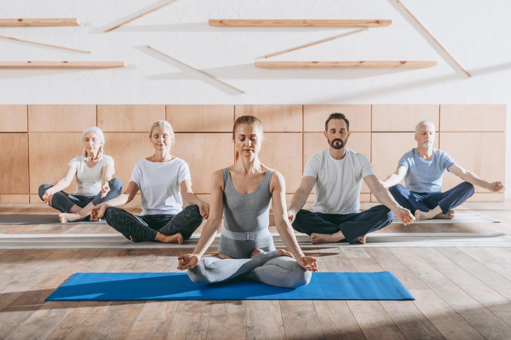 gruppo di anziani che praticano yoga con istruttore in posa di loto su stuoie in studio
 - Foto, immagini