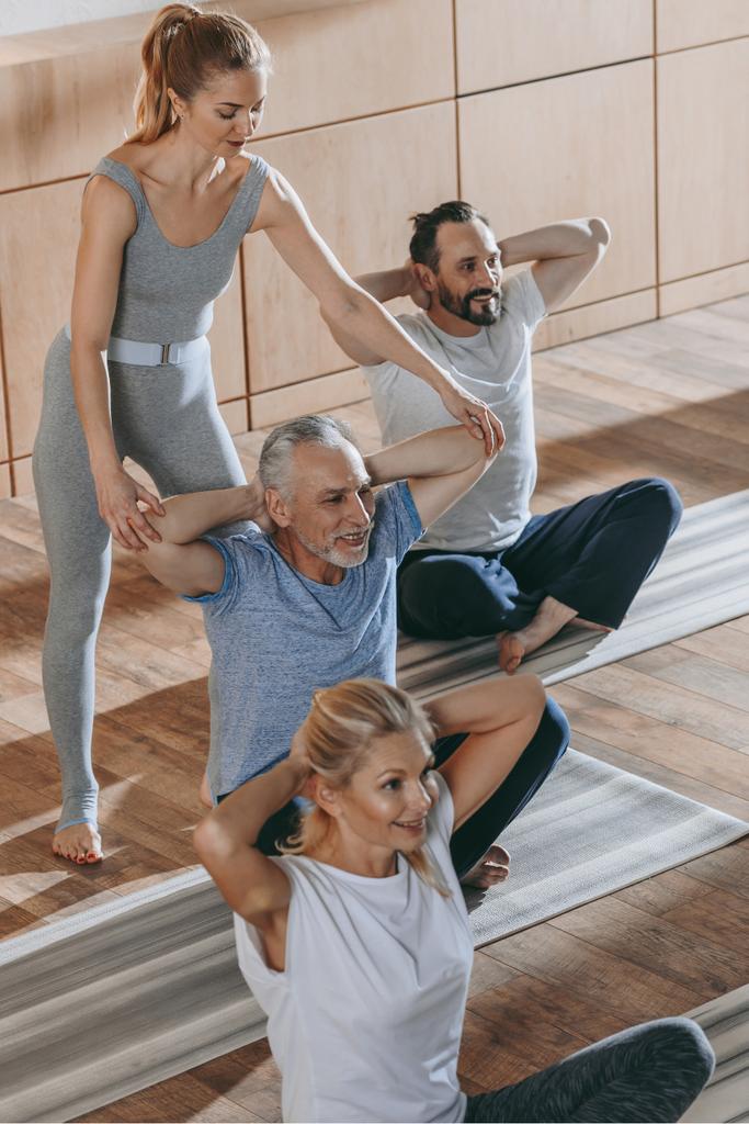 vrouwelijke instructeur opleiding senior mensen zitten op yoga matten in de fitness-studio - Foto, afbeelding