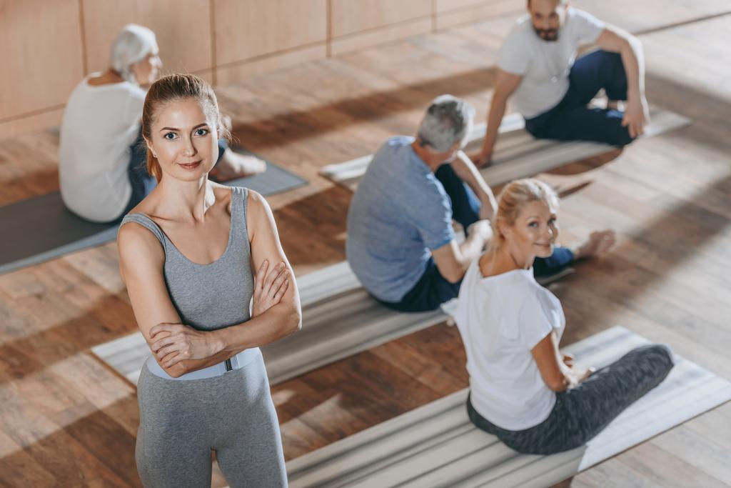 visão de alto ângulo do instrutor feminino olhando para a câmera enquanto as pessoas idosas se exercitam em tapetes de ioga
 - Foto, Imagem