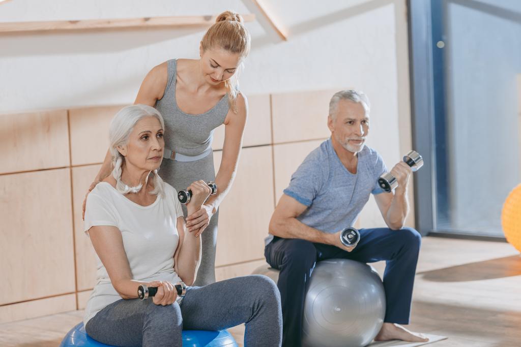 instructeur aidant les personnes âgées à s'entraîner avec des haltères et des balles de fitness dans un studio de fitness
 - Photo, image
