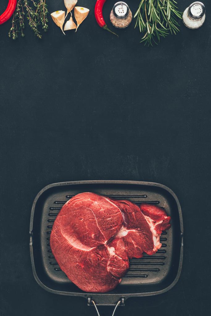 pohled shora na tatarský biftek na grilovací pánvi s kořením na černém povrchu - Fotografie, Obrázek