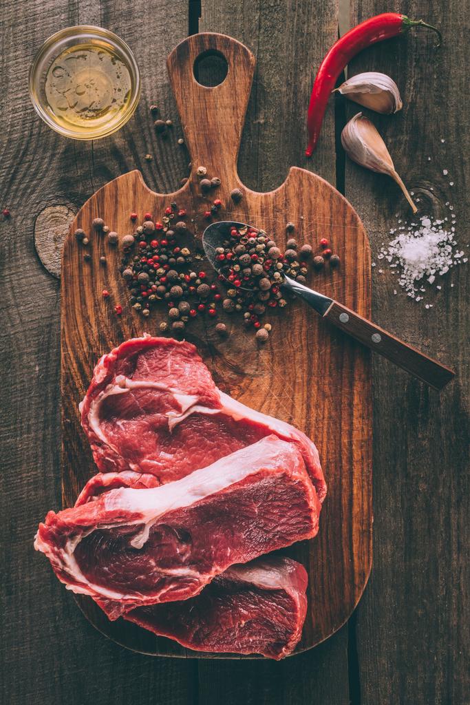top view of heap of steaks with spices on wooden cutting board - Photo, Image