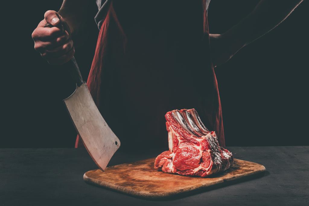 Rzeźnik z tasakiem i surowego mięsa na drewnianą deską do krojenia - Zdjęcie, obraz