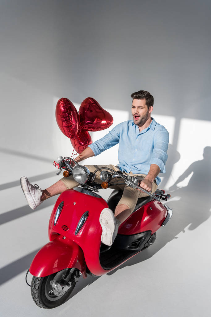 joven con globos en forma de corazón a caballo scooter rojo
 - Foto, imagen