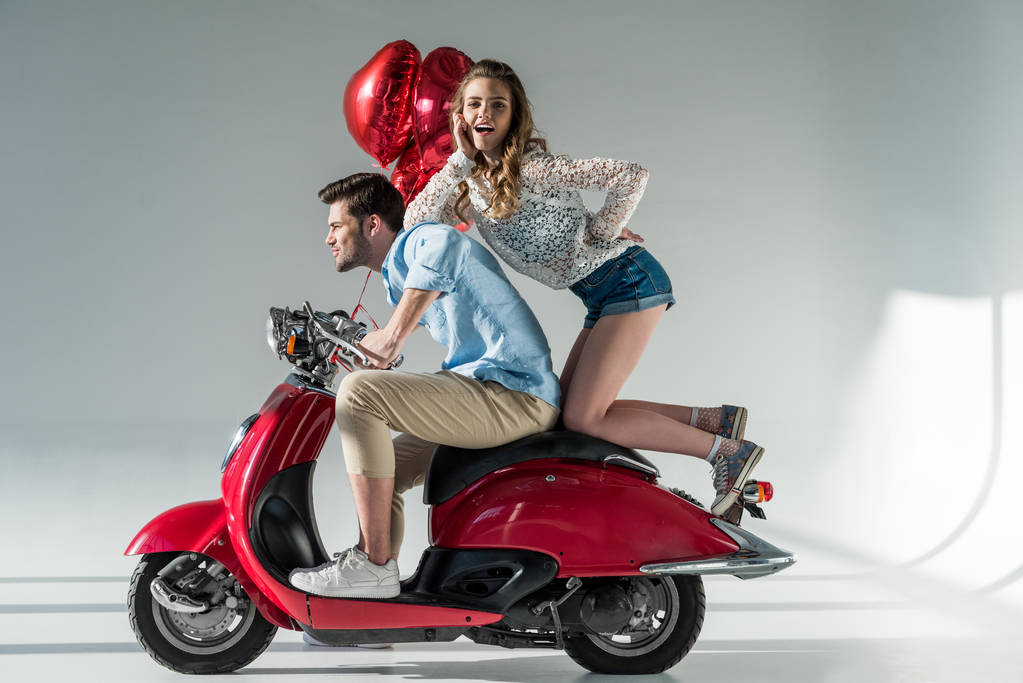 side view of young couple in love with heart shaped balloons on red scooter - Photo, Image