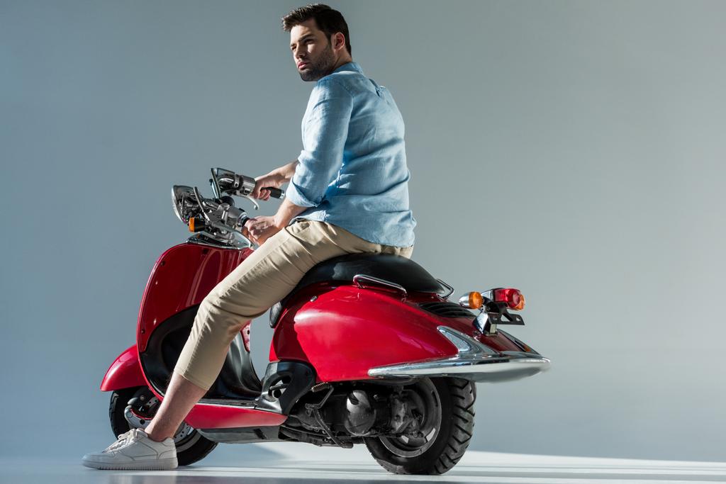 Вид сбоку модного молодого человека, катающегося на красном скутере
 - Фото, изображение