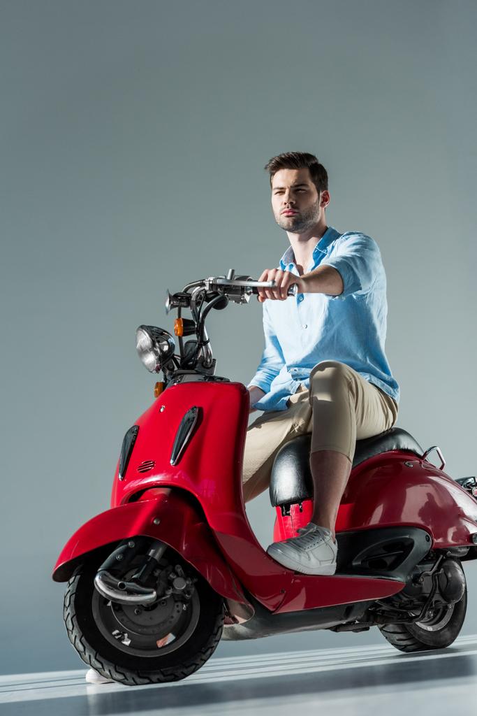 вдумливий молодий чоловік в модному одязі, сидячи на червоному скутері
 - Фото, зображення