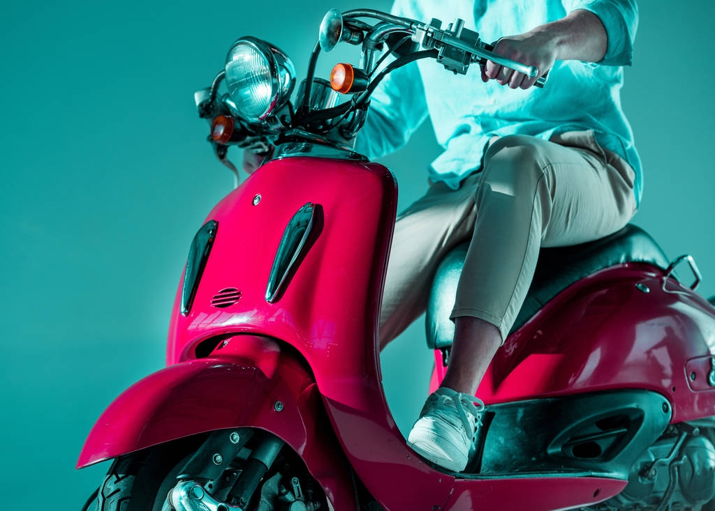частичный вид человека в стильной одежде, сидящего на красном скутере
 - Фото, изображение