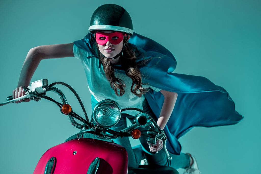 portrait of woman in superhero costume and protective helmet riding red scooter - Photo, Image