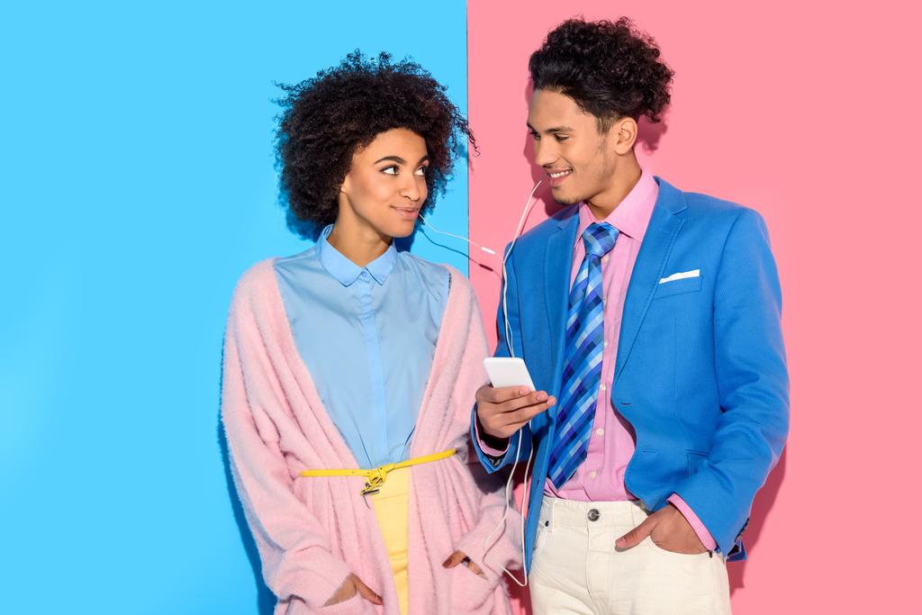 Νεαρό ζευγάρι να ακούτε μουσική στο smartphone σε ροζ και μπλε φόντο  - Φωτογραφία, εικόνα