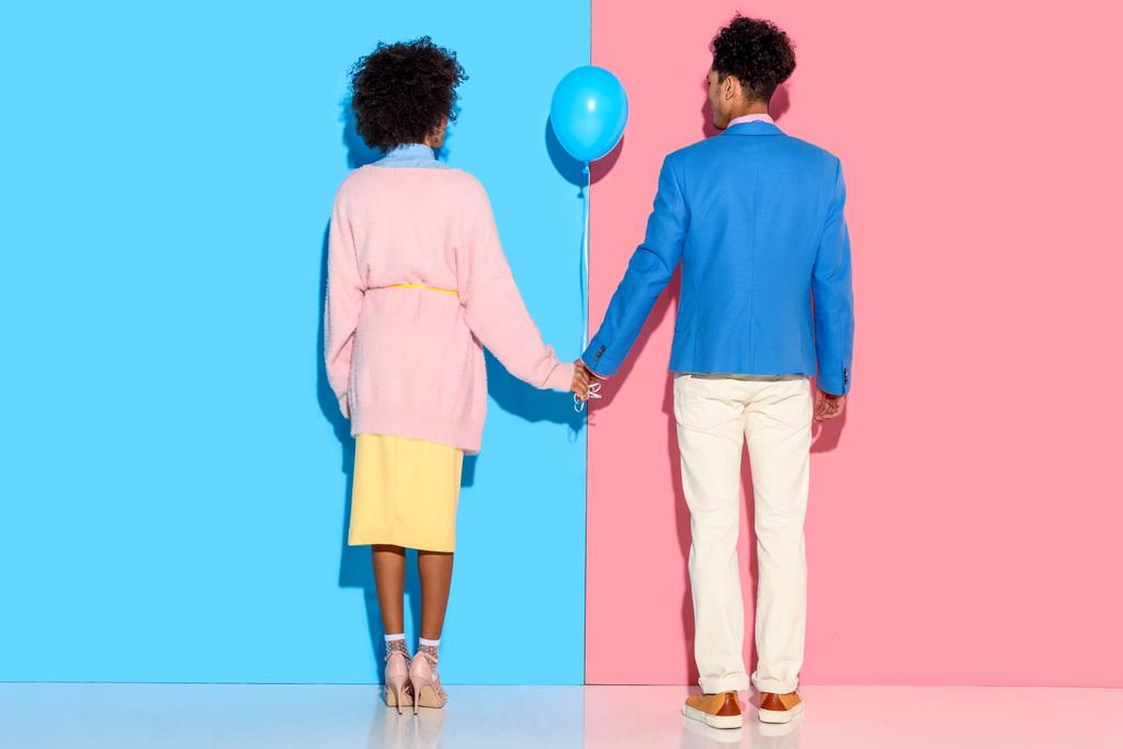Achteraanzicht van jonge paar hand in hand met de luchtballon op roze en blauwe achtergrond  - Foto, afbeelding