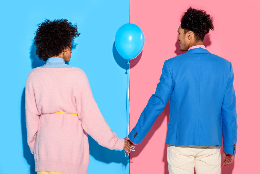 Вид ззаду пари, що тримає руки з повітряною кулею на рожевому та синьому тлі
  - Фото, зображення