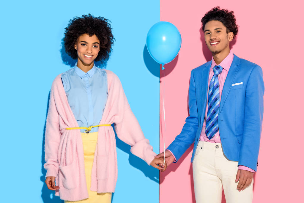 Young couple holding hands with air balloon on pink and blue background - Photo, Image