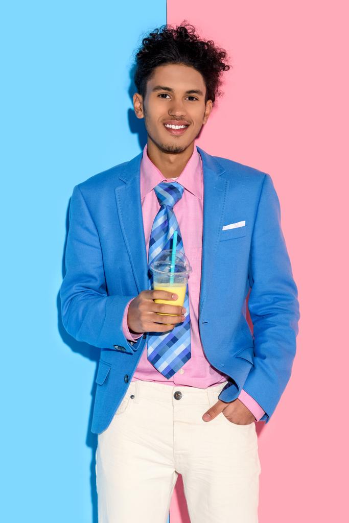 mosolyogva pohár gyümölcslé, rózsaszín és kék falnak afrikai amerikai férfi portréja - Fotó, kép