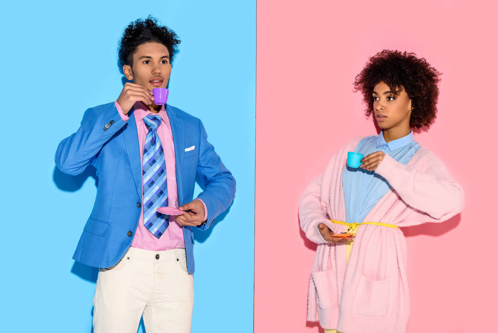 stylisches afrikanisch-amerikanisches Paar mit Spielzeug-Teetassen mit rosa und blauen Wandhintergrund - Foto, Bild