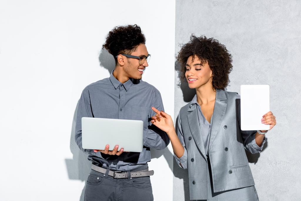 Молодой африканский американский бизнесмен с ноутбуком и бизнесвумен с планшетом в руке на сером и белом фоне
  - Фото, изображение