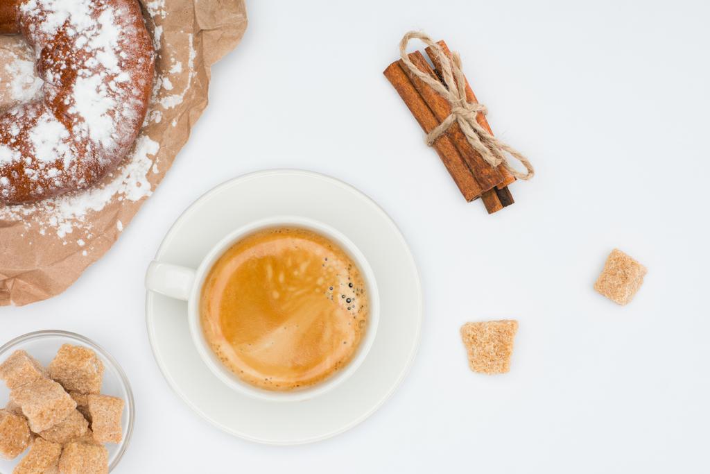 Oberseite der Tasse Kaffee mit Untertasse und braunem Zucker, Gebäck und Zimtstangen mit Seil isoliert auf weiß gebunden  - Foto, Bild
