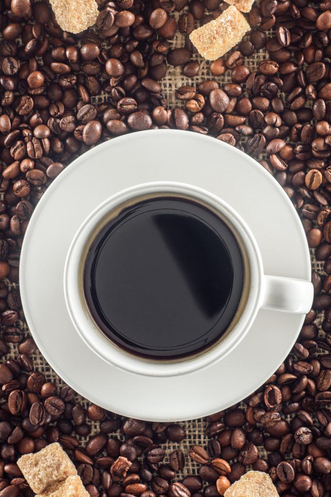 top view of cup of coffee, roasted coffee beans and brown sugar on sackcloth  - Photo, Image