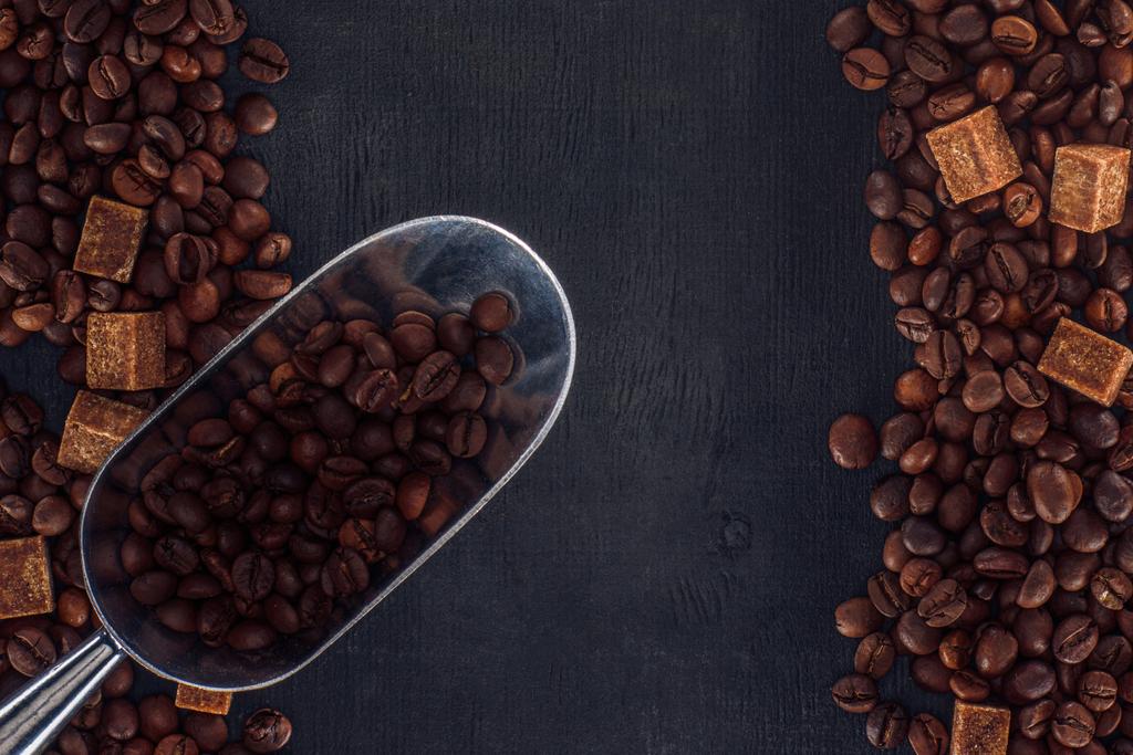 κάτοψη του φρυγμένους κόκκους καφέ με μαύρη ζάχαρη και σέσουλα στο μαύρο  - Φωτογραφία, εικόνα