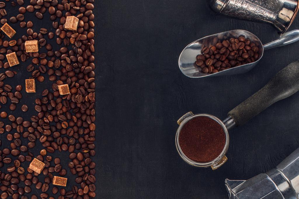 bovenaanzicht van gebrande koffiebonen, suiker, scoop, koffie knoeien, koffiepot en koffie-/ theevoorzieningen op zwart   - Foto, afbeelding