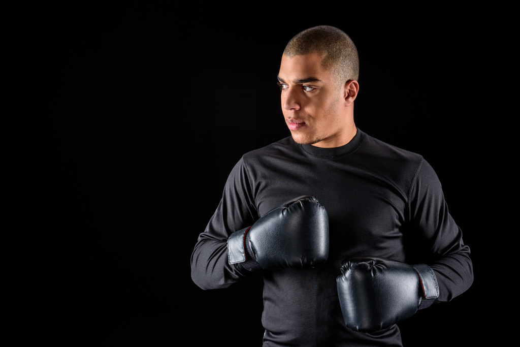 jonge Afro-Amerikaanse bokser in sportkleding en zwarte handschoenen geïsoleerd op zwart - Foto, afbeelding