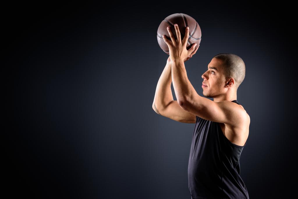 Zijaanzicht van Afro-Amerikaanse basketballer gooien van de bal op zwart - Foto, afbeelding