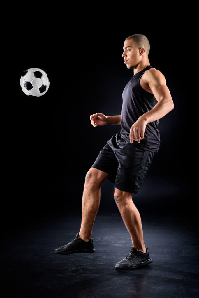 красивий афроамериканський футболіст стрибає м'яч на нозі на чорному
 - Фото, зображення