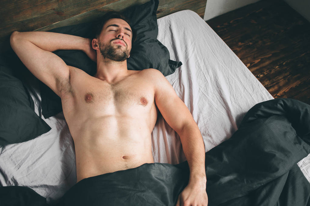 Ritratto di modello maschile in forma addormentato nella lussuosa camera da letto bagnata dalla luce calda della finestra del mattino
 - Foto, immagini