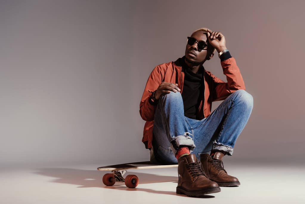 stylischer junger afrikanisch-amerikanischer Skateboarder sitzt auf dem Longboard - Foto, Bild