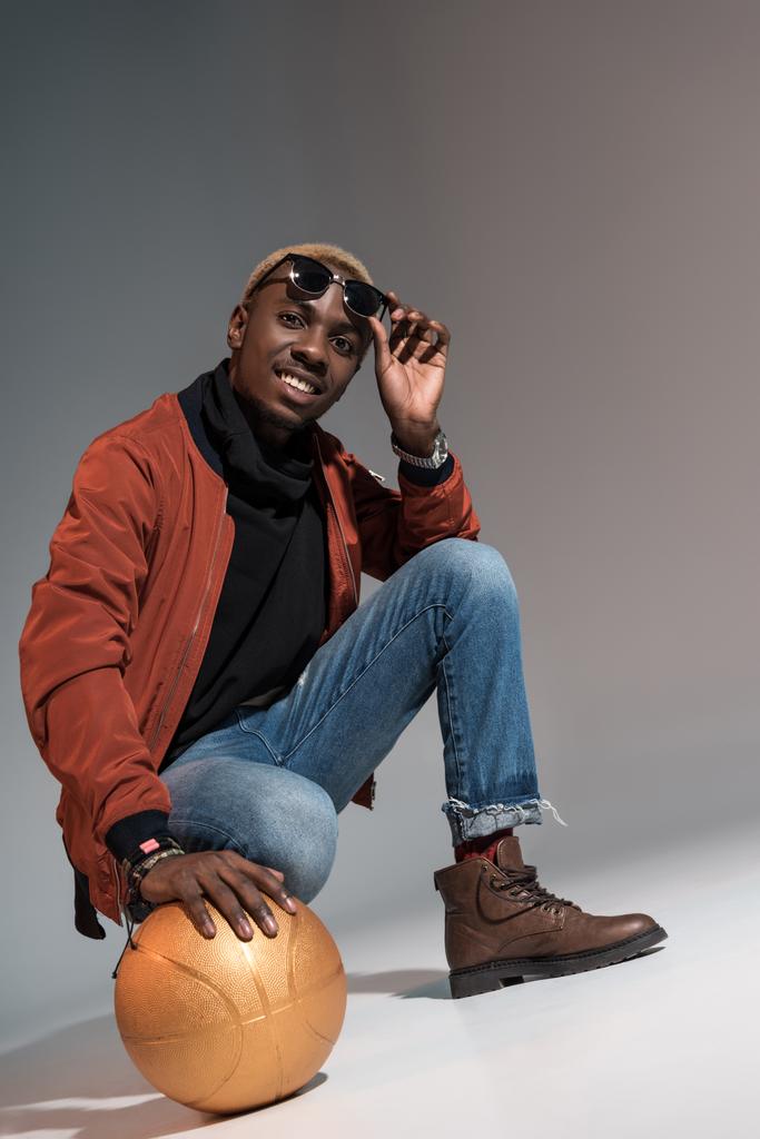 Tyylikäs nuori afrikkalainen amerikkalainen hymyilevä mies pitäen koripalloa lattialla
 - Valokuva, kuva