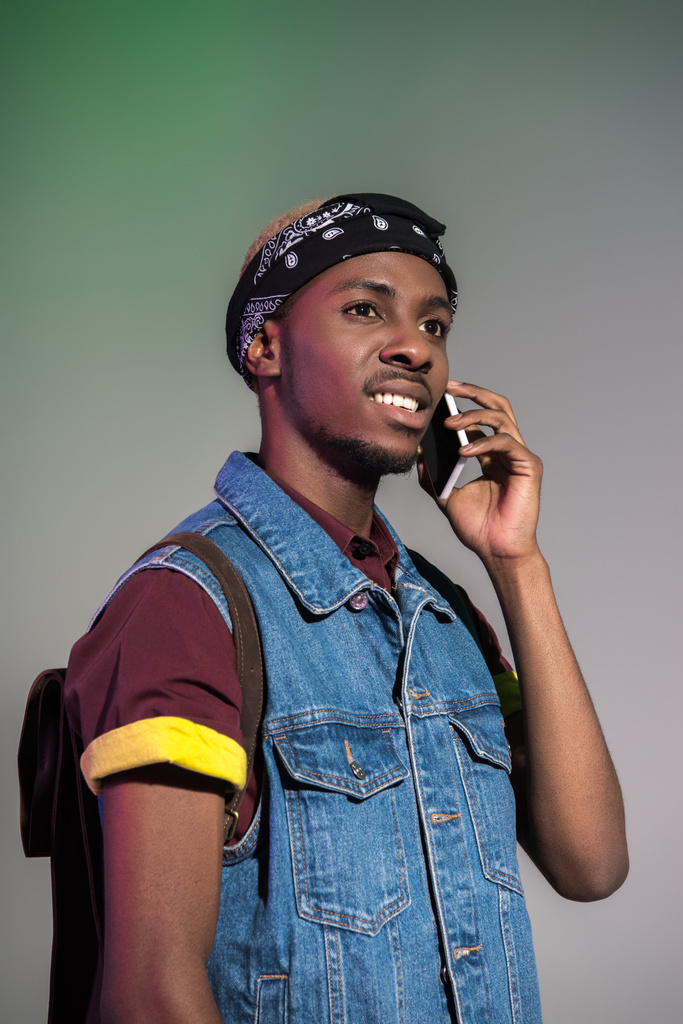 guapo joven afroamericano hombre hablando en el teléfono inteligente y mirando hacia otro lado aislado en gris
 - Foto, Imagen