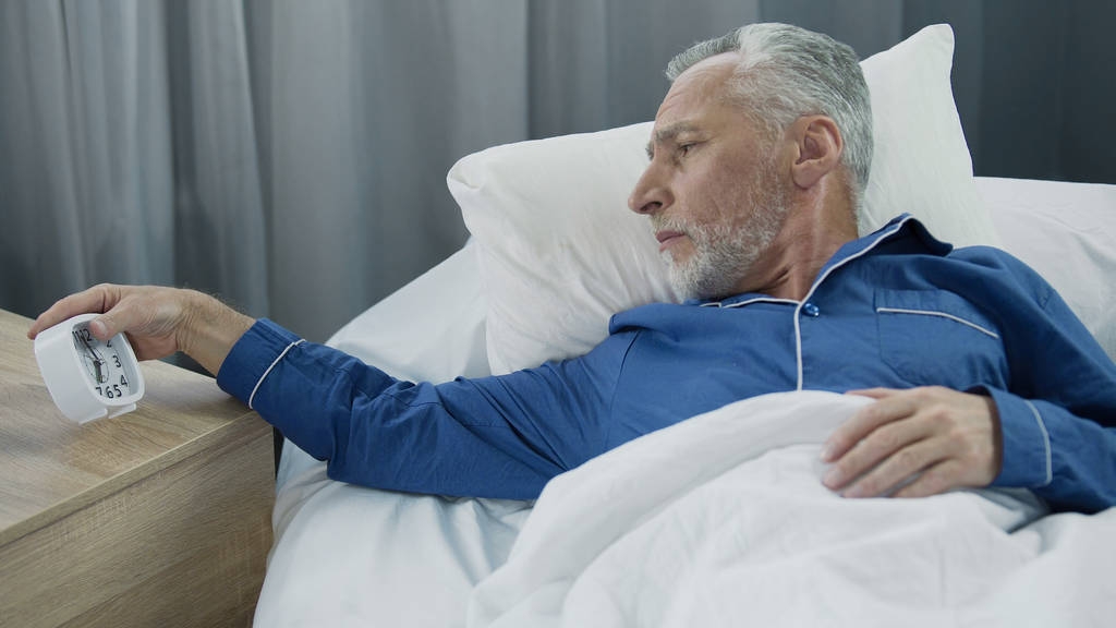 Anciano oyendo despertador, renuente a despertar, falta de sueño y energía
 - Foto, Imagen