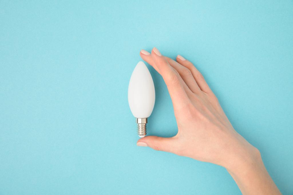 частковий вид жінки, що тримає лампочку в руці ізольовано на синьому
 - Фото, зображення