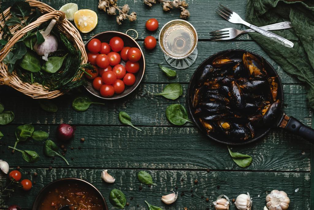 トマト、ハーブと素朴なテーブルの上にワイン鍋にて調理済みムール貝のシェルの平面図 - 写真・画像